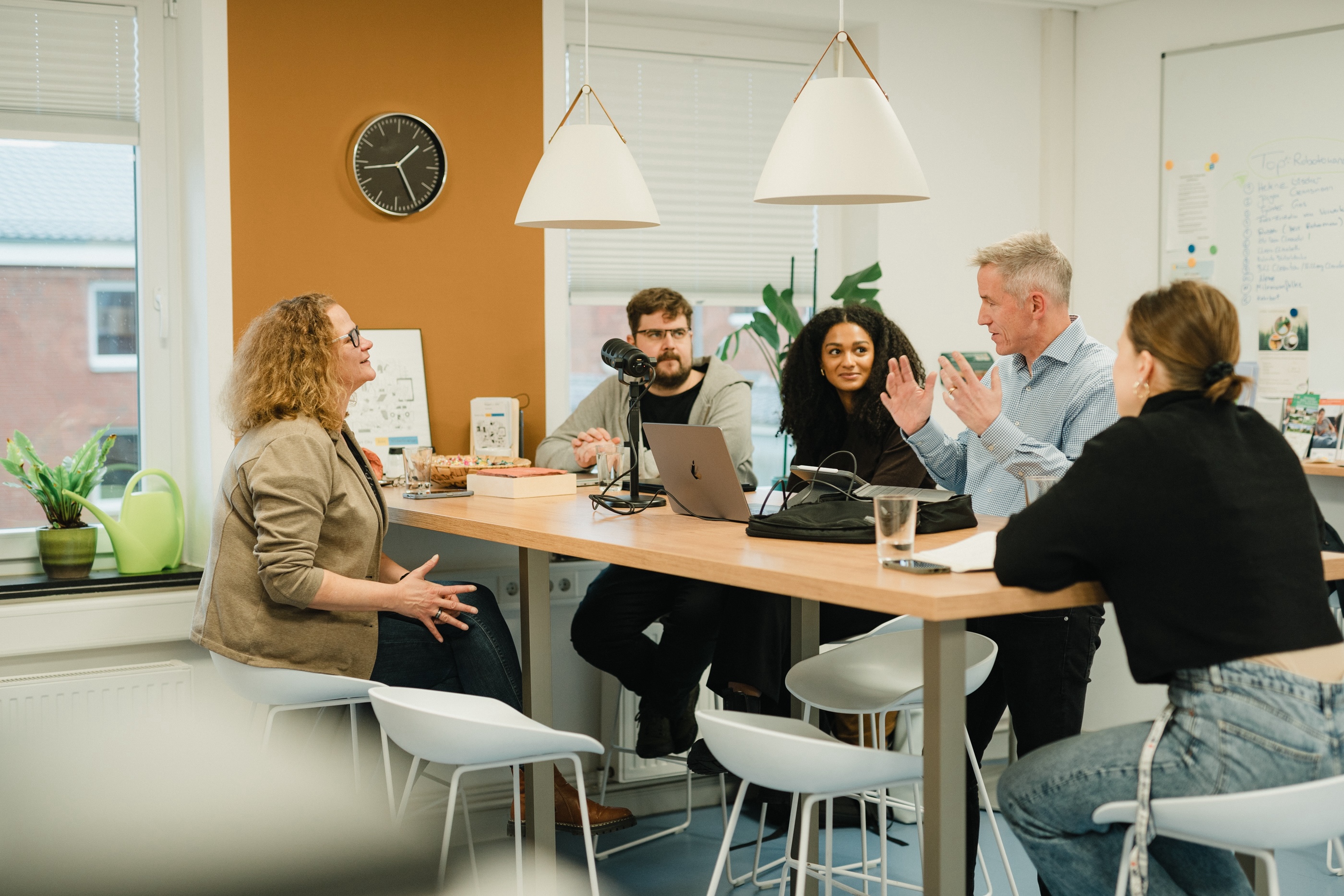 Fünf Personen sitzen bei einer Besprechung um einen Tisch und diskutieren miteinander