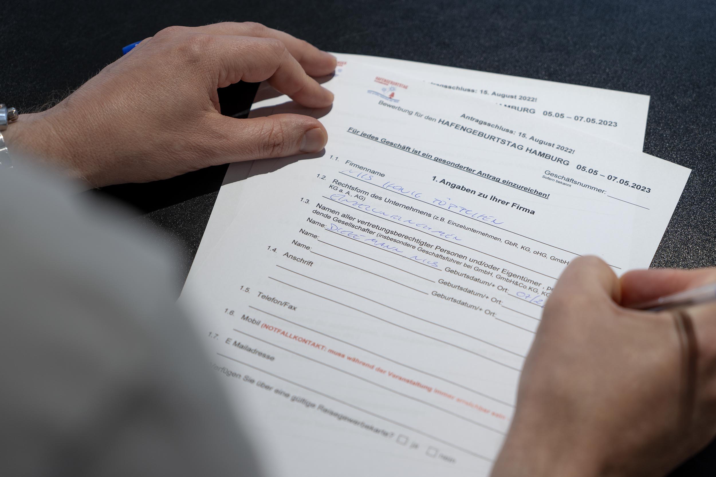 Person füllt ein mehrseitiges Papierformular für den Hafengeburtstag der Stadt Hamburg von 2023 handschriftlich aus